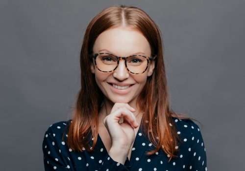 happy-delighted-young-woman-keeps-one-hand-under-chin-smiles-happily-wears-transparent-glasses_t20_YEPyl1